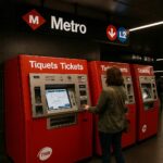 Ticket vending machines inside a Barcelona Metro station, with passengers using the machines and clear bilingual signage visible.